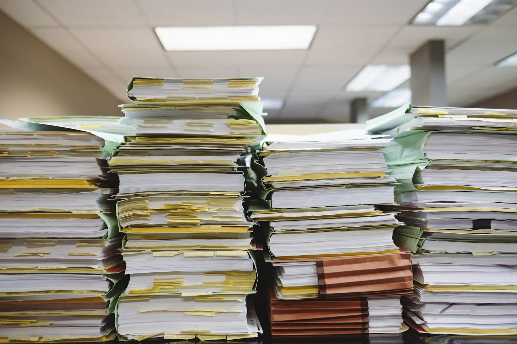 Stacks of tabbed file folders and printed documents piled on an office desk