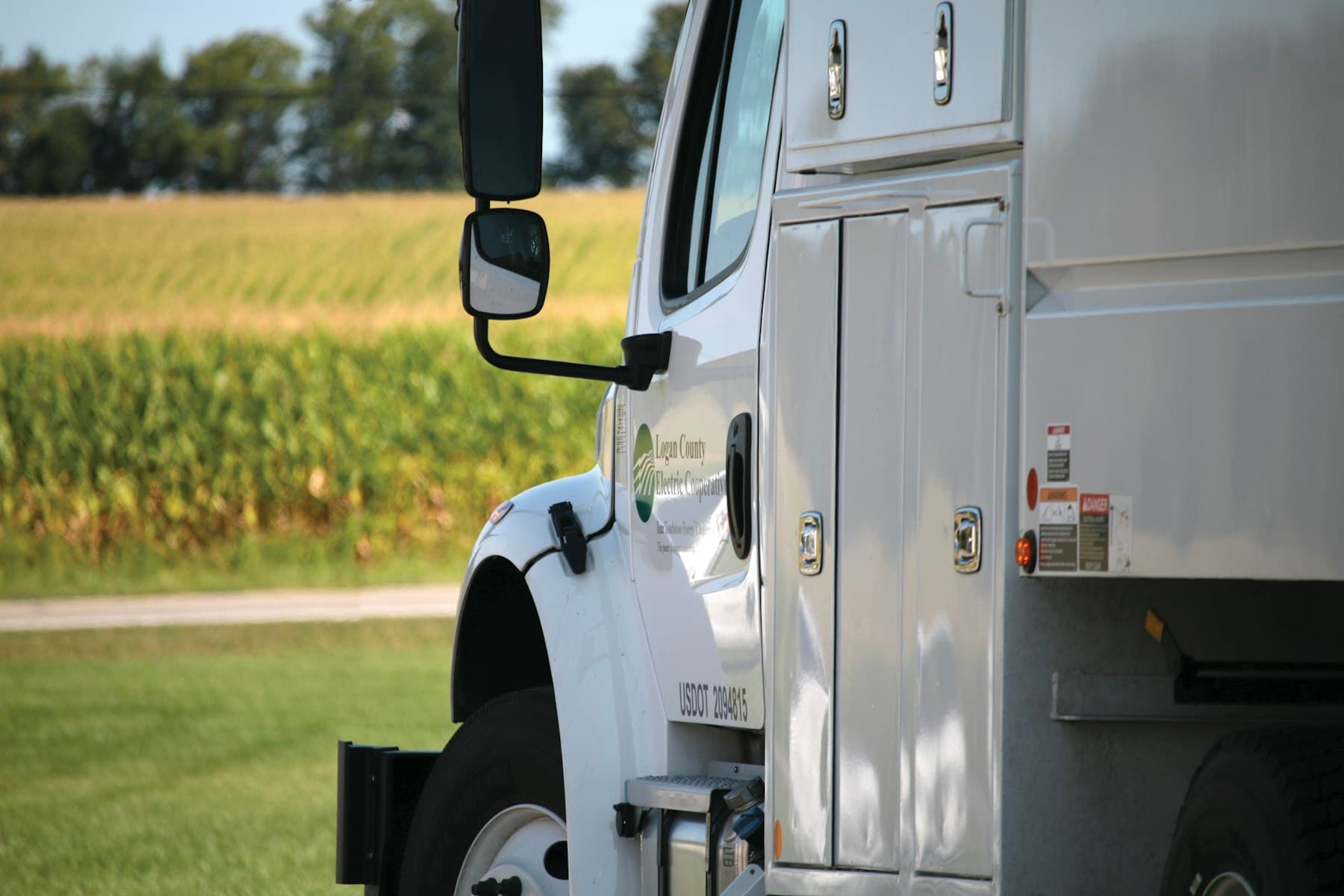 White contractor work truck with a utility body parked beside a green field