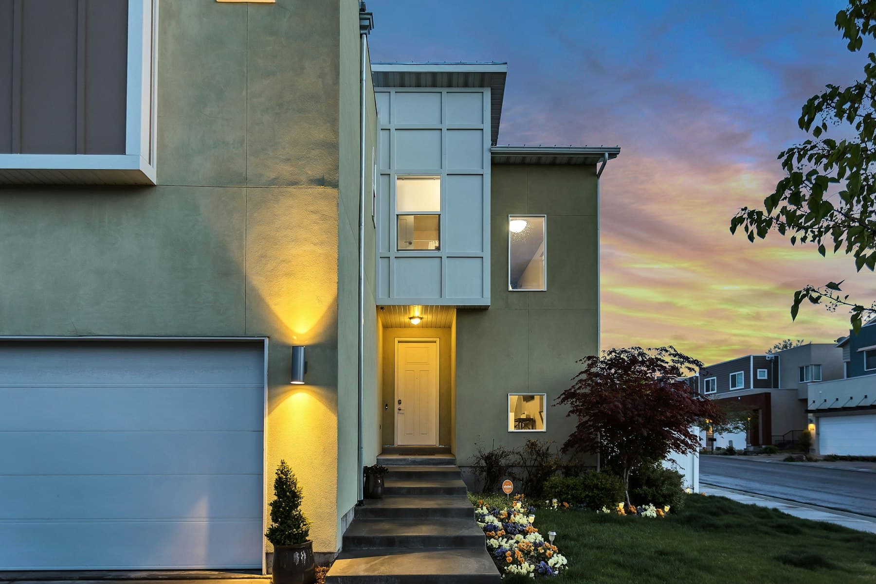Modern stucco house at dusk with warm entry lights and a sunset sky