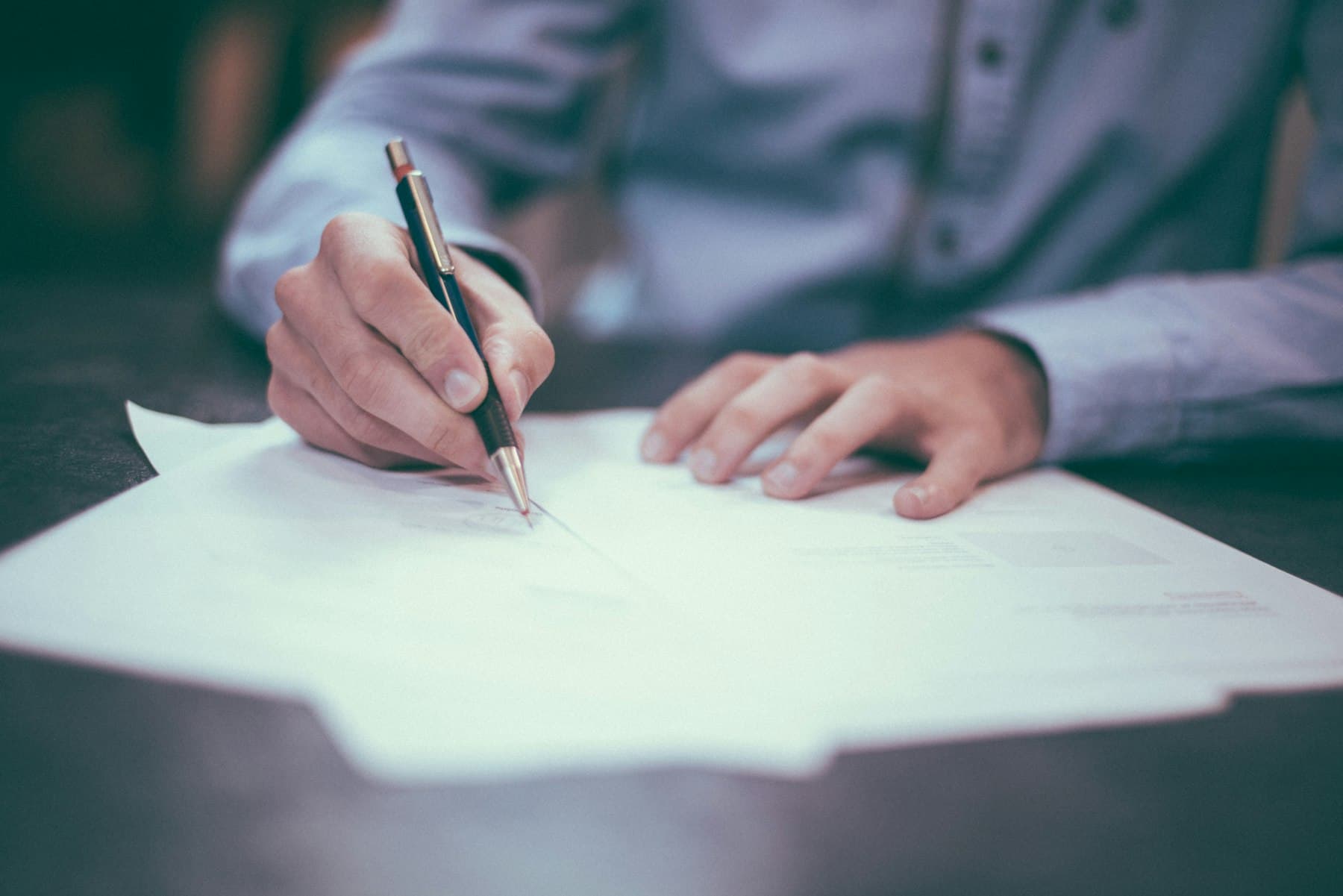 Hands signing paperwork with a fountain pen at an office desk