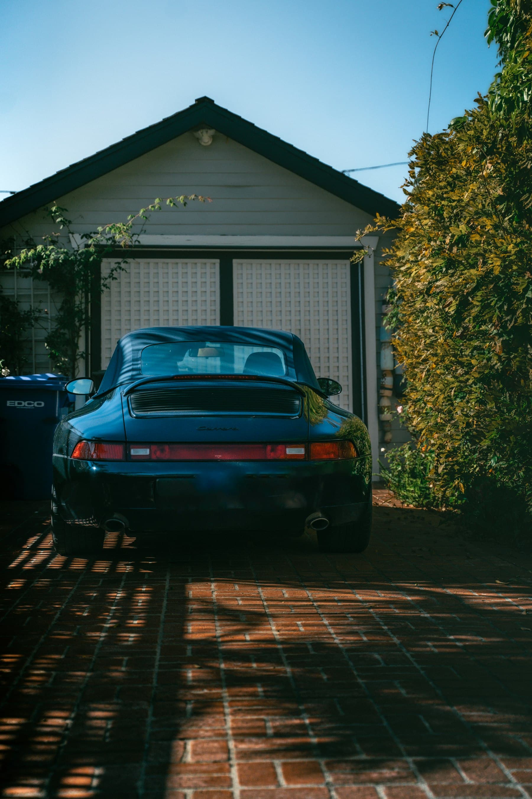 Blue coupe parked on a brick driveway in front of a home garage