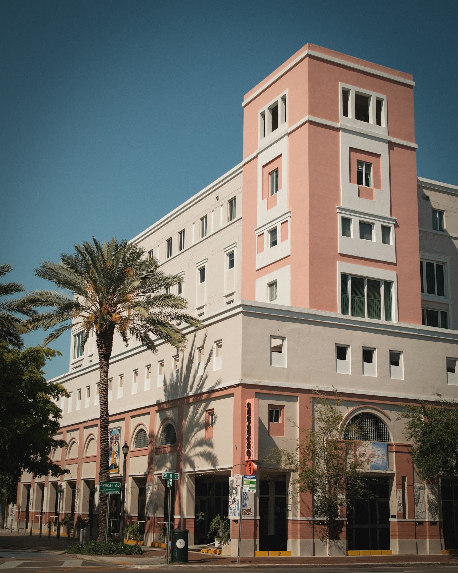 Pink stucco commercial building on a sunny street corner with a palm tree out front