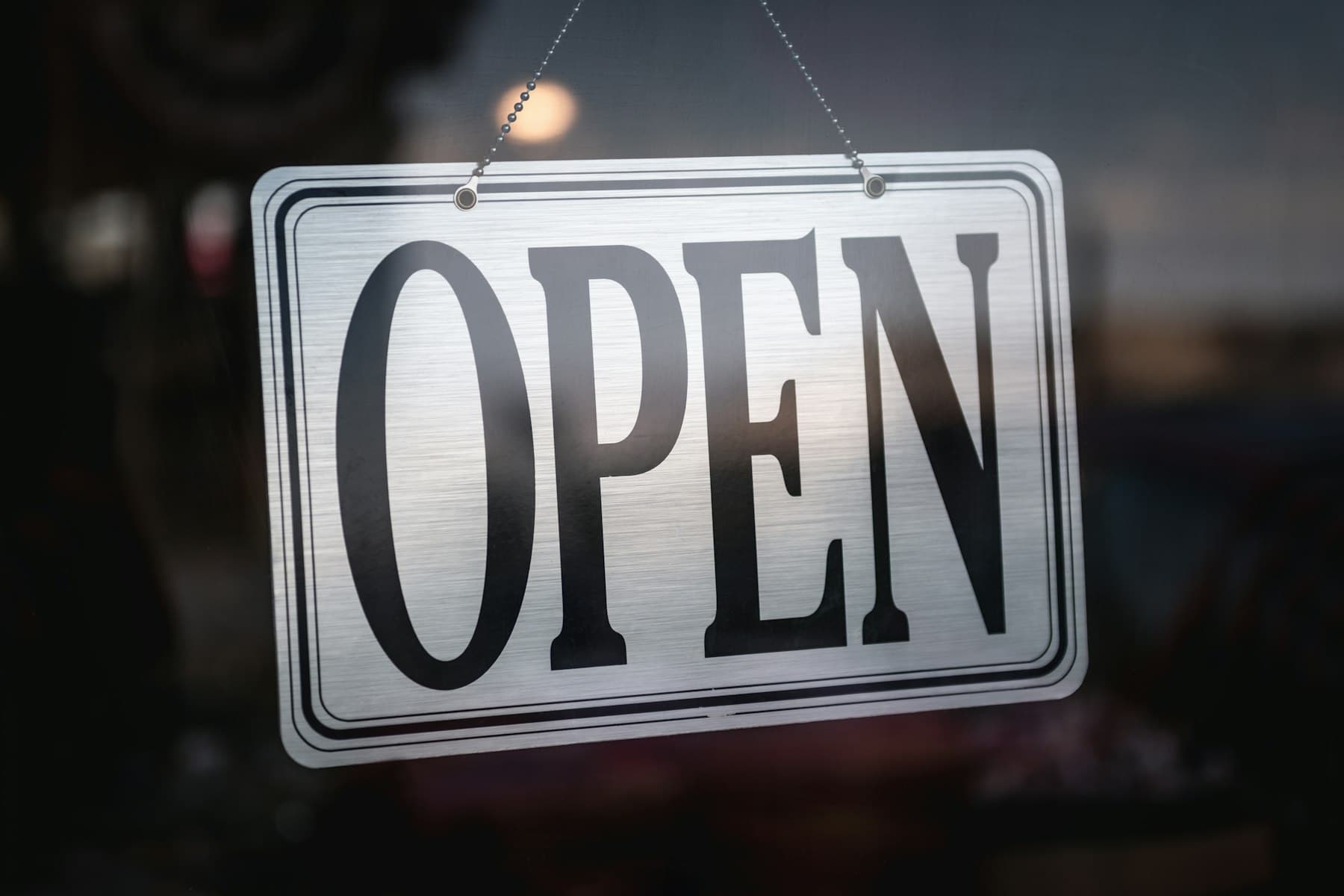 Open sign hanging inside the glass door of a small shop at opening time
